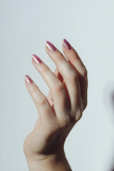 A close-up of a hand with pearl pink nails against a clean white background
