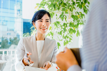 明るい室内で顧客にプレゼンテーション資料の説明をして営業する30代の笑顔の女性