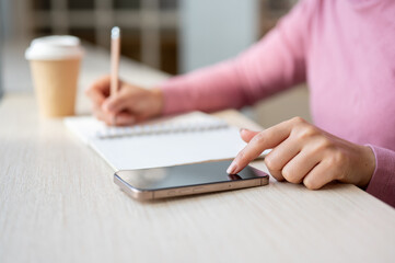 A woman using her smartphone, which is placed on the table, while working in a coffee shop.
