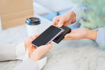 お店でコーヒーをスマートフォンのタッチ決済で購入する女性の手元