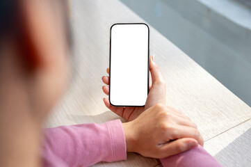 A woman sitting in a coffee shop on a bright day, reading messages or news on her smartphone.