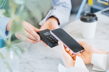 飲食店でテイクアウトコーヒーをスマートフォンのタッチ決済で購入する女性の手元