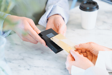 お店でコーヒーをクレジットカードのタッチ決済で購入する女性の手元