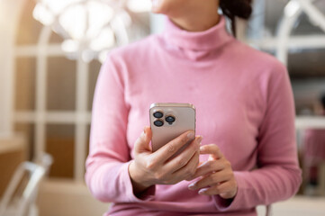 Fototapeta premium A thoughtful Asian woman gazes out the window while holding a smartphone, relaxing in a coffee shop.