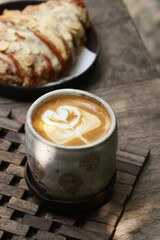 a cup of coffee with latte art with a plate of croissant behind