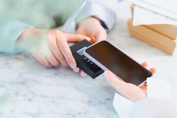 お店の商品をスマートフォンのキャッシュレス決済のタッチで買う女性の手元