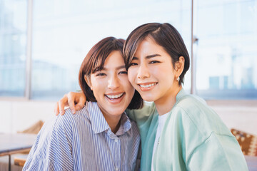 笑顔で肩を抱くカメラ目線の30代の2人の友達の女性のカメラ目線