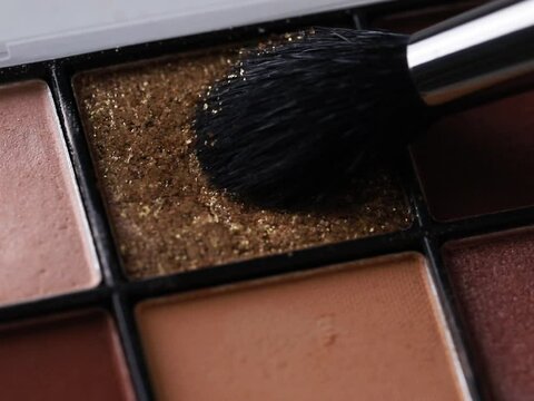A close-up of beige tone eyeshadow palette showcasing with a makeup brush gently hovering over it