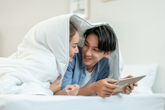 Asian young couple watching movie on digital tablet in bedroom at home. 