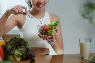 Smiling sportswoman enjoying a healthy vegetable salad filled with fresh tomatoes and crisp...