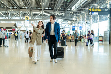 Asian businessman and woman walking in airport terminal to boarding gate.