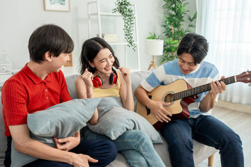 Diverse Asian friends playing guitar and singing in living room at home. 