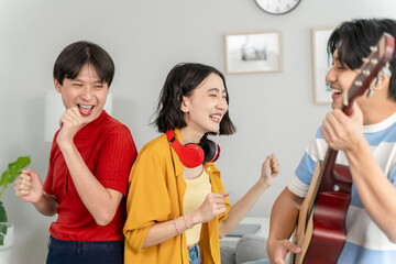 Diverse Asian friends playing guitar and dancing in living room at home. 