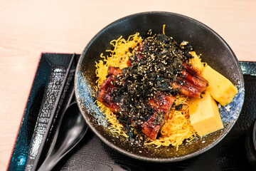 close up of Japanese egg roll and grilled eel rice Unadon on a black tray with chopsticks