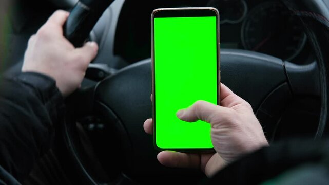 Man using phone with blank green background while driving. Road safety. Automotive technologies. GPS navigation. Mobile applications for drivers. Using gadgets while driving. Smartphone chroma key