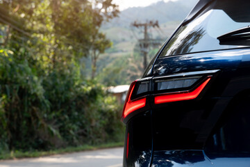 Rear side of dark with turn on brake light. side of car on aspahlt road with tree and grass in the countryside.