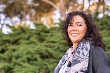 Naklejka premium Confident. Stylish woman with a perfect smile enjoys the freedom of nature. Surrounded by lush greenery and trees in a serene outdoor setting. Embracing the tranquility and beauty of the environment