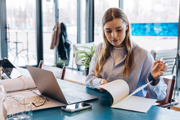 Businesswoman reading documents and working on laptop in modern office