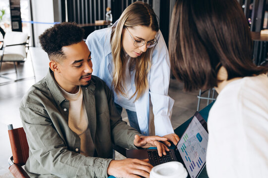 Diverse team of software developers collaborating on user interface design on laptop in modern office