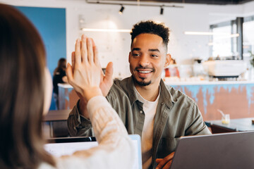 Two happy business colleagues giving high five in cafe