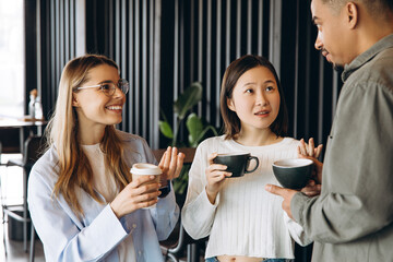 Diverse colleagues enjoying coffee break, discussing work in modern office space