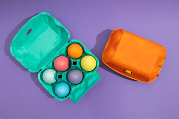 Top view of colorful eggs in a blue painted basket next to an orange one on a purple background. Easter painted eggs