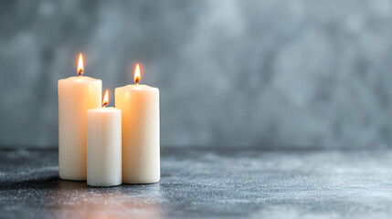 Three candles burning on grey surface, peaceful background