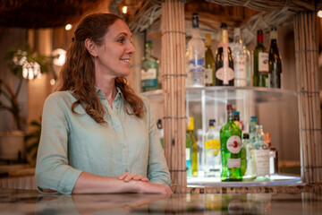 happy woman smile stands behind a bar counter in a tropical or rustic-themed includes a few plants, enhancing the natural and cozy atmosphere holidays concept.