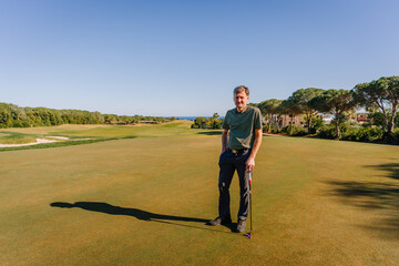 Obraz premium A golfer standing on a sunny golf course with a club in hand, surrounded by greenery, sand bunkers, and a clear blue sky.