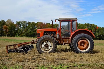 Obraz premium Vintage red tractor in autumn field with blue sky.