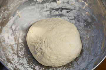 A round, raw dough sits in a metal bowl
