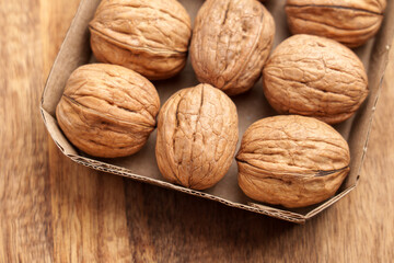 Organic walnuts in paper pack on wooden table. Unpeeled nuts with nutshell in cardboard box. Top view. 