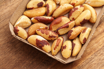Dried Brazil nuts in a cardboard tray on wooden table. Top view.
