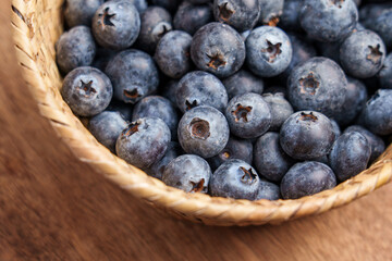 Ripe blue berries in a rustic woven basket on wooden surface. Fresh natural superfood. Source of vitamins and antioxidants. Top view