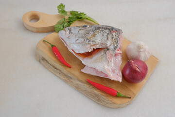 Raw golden snapper heads ready for cooking with some spices on wooden cutting board