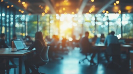 A bright, modern workspace filled with people collaborating, working on laptops, and enjoying natural light filtering through large windows.