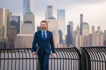 Fototapeta premium Business man in New York City. Man in suit at NYC financial district. Financial Manhattan. Business man with laptop at cityscape in NYC. Business man in suit outdoor. Business Lifestyle. Businessman
