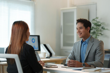 Happy businessman listening to his female colleague during a meeting in a modern office, they are discussing work and analyzing graphs on computer screen