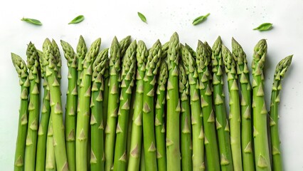 Fototapeta premium A top-down view of vibrant green asparagus spears neatly arranged on a white background with scattered leaves, emphasizing their natural freshness and crisp texture.