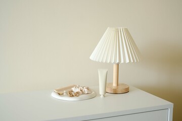 An elegant modern table Lamp featuring Neutral Decor Accents , woman accesseries on white concrete plate on white desser in light room.
