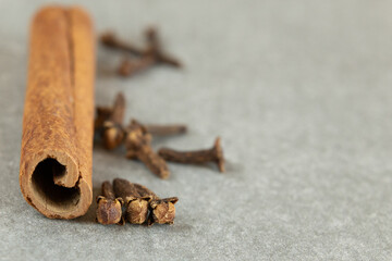 A close-up of a cinnamon stick and dried cloves on a grey surface. 