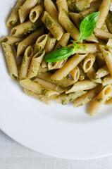 Penne pasta with pistachio pesto with a sprig of basil in a white plate on the table. Italian cuisine concept. Vertical orientation. Selective focus. Top view