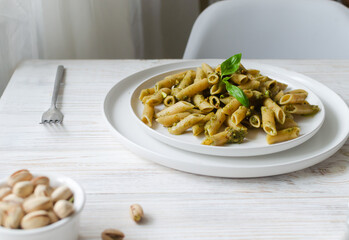 Penne pasta with pistachio pesto with a sprig of basil in a white plate with a fork on a table in a restaurant. Italian cuisine concept. Horizontal orientation. Selective focus.