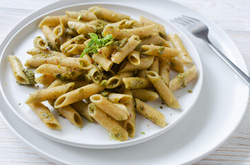 Penne pasta with pistachio pesto with a sprig of basil in a white plate with a fork on a table in a restaurant. Italian cuisine concept. Horizontal orientation. Selective focus.