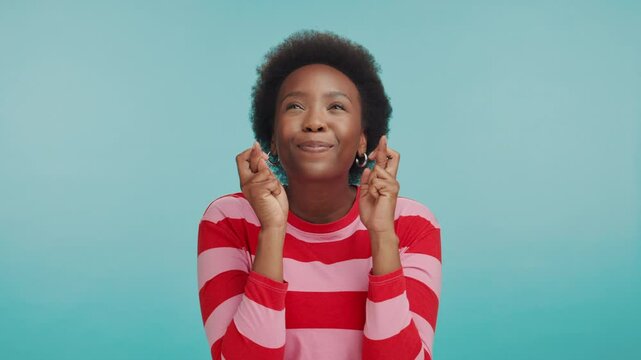 Hope, fingers crossed and face of woman in studio with smile, good luck and opportunity to win. Wish, praying and portrait of happy African person with choice, thinking or optimism on blue background