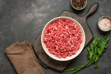 Raw mince beef with spices, ground meat in bowl on wooden cutting board, dark grunge background, top view, flat lay