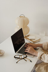 Hands Typing on Laptop in Minimalistic Home Office Setup with Notebooks and Paper Lantern