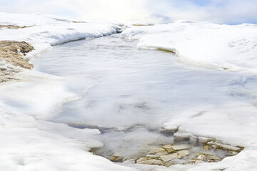 A partially frozen river with melting ice revealing the rocky bottom, symbolizing the transition from winter to spring..