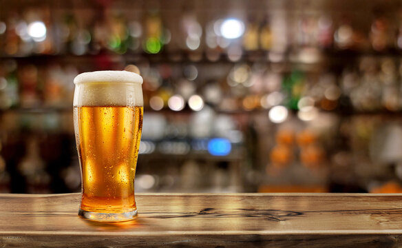 Glass of chilled beer on wooden bar tabletop and blurred brightly lit bar interior in the background. Clipping path for table.