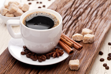 Cup of coffee on white plate, several coffee beans and brown sugar on wooden table close up. Top view.